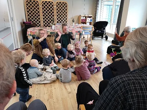 Små børn sidder sammen med voksne og leger 